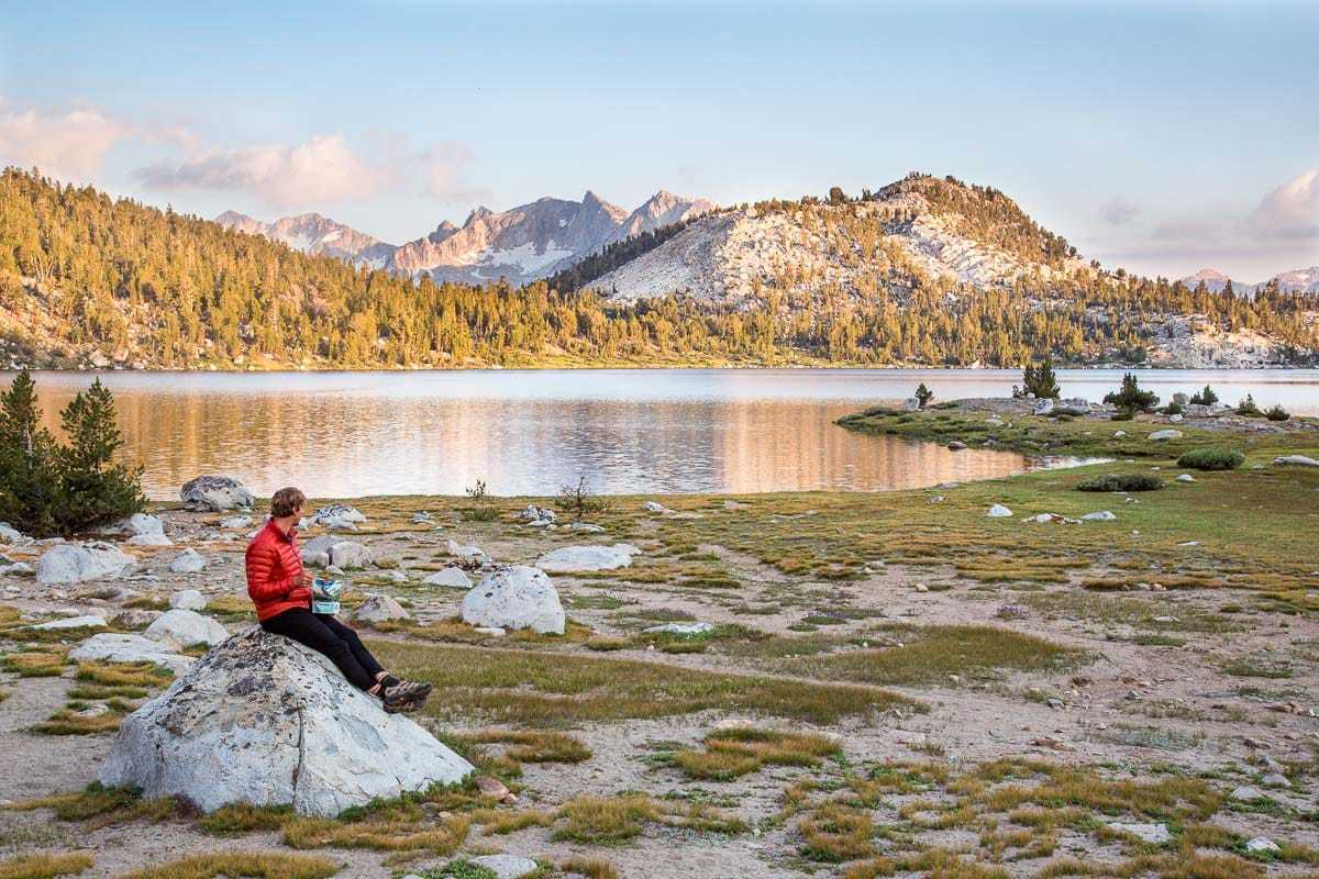 Ο Michael κάθεται σε έναν βράχο με μια λίμνη και βουνά στο βάθος