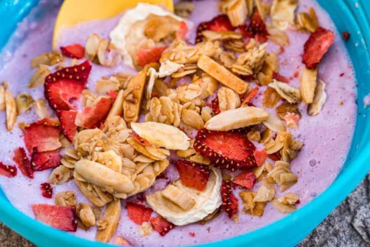 Tutup yogurt, granola dan buah-buahan dalam mangkuk biru