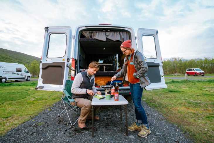 Una pareja cocinando delante de una furgoneta camper