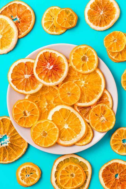 Сушени портокалови резени върху чиния, заобиколени от дехидратирани портокалови резени.