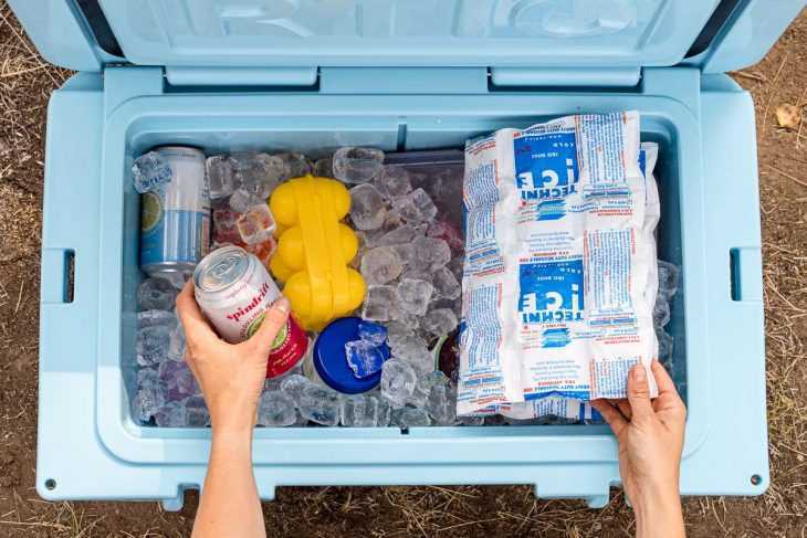 Mani che si protendono in un frigorifero blu pieno di ghiaccio per prendere una lattina