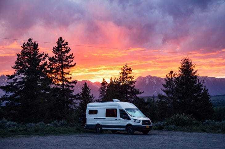 Sebuah campervan diparkir dengan matahari terbenam dan pegunungan Teton sebagai latar belakang