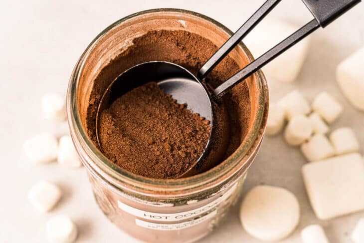 Изглед отгоре на буркан, пълен с горещ какаов микс с мярка от ¼ чаша, загребваща сместа за домашно приготвено горещо какао.