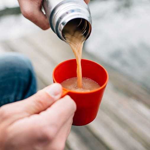 Menuangkan teh latte dari termos ke dalam cangkir kecil berwarna merah