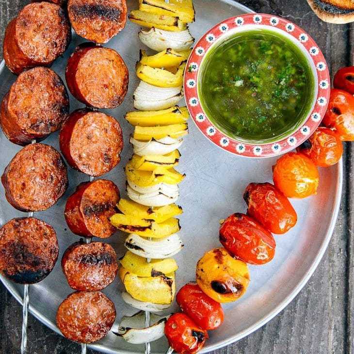 Un festin de barbecue vibrant comprenant des saucisses grillées juteuses, des brochettes de légumes colorées avec des oignons, des poivrons et des tomates, ainsi qu