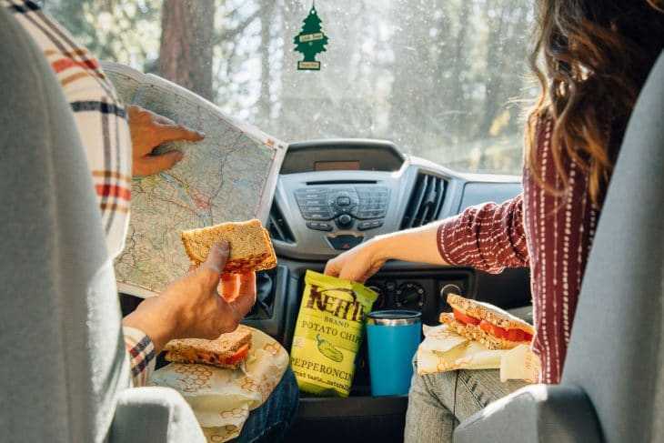 Megan sedi v kombiju in seže v vrečko čipsa. Michael drži sendvič in bere zemljevid