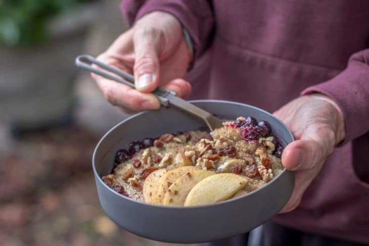 Ținând în mână un bol de terci de quinoa la micul dejun cu mere.