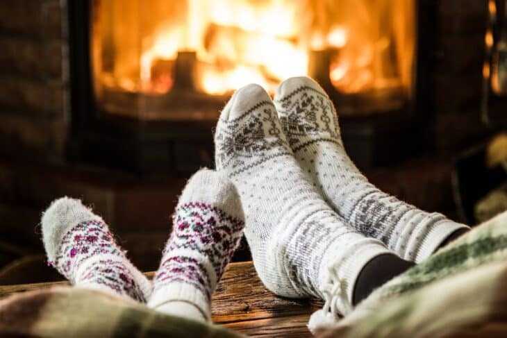 Dva páry nohou na sobě teplé fuzzy ponožky s krbem v pozadí.
