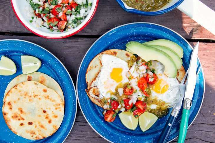 Mavi kamp tabaklarındaki tortillaların üzerinde yumurta, salsa ve avokado.