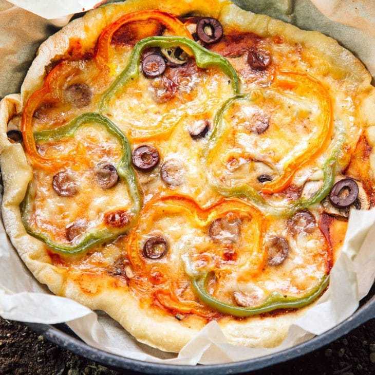 Pizza acoperită cu brânză și ardei gras într-un cuptor olandez