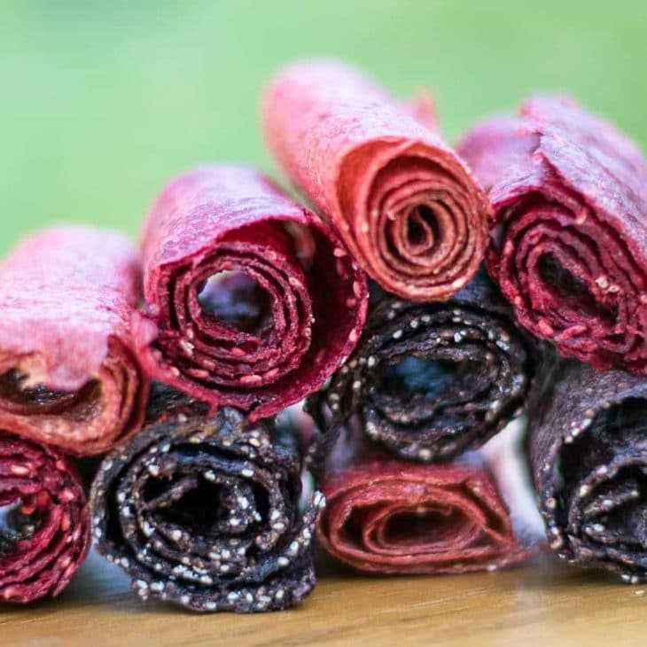 Detailní záběr na živé, domácí ovocné kožené rolky v červené a tmavě fialové barvě, což naznačuje chutnou a přirozenou možnost občerstvení.