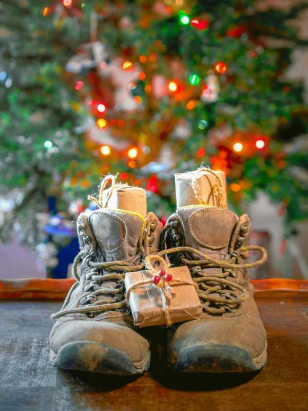 Sepasang sepatu hiking berisi hadiah. Sebuah pohon Natal ada di latar belakang