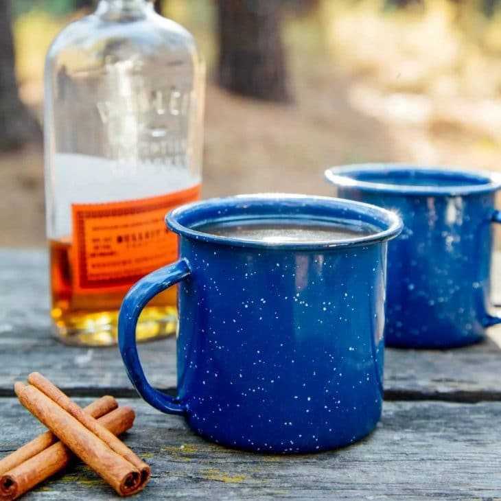 Una taza de esmalte azul junto a una botella de whisky.