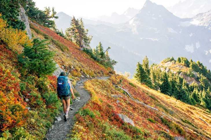 Femeie care face drumeții în Munții Cascade cu frunziș de toamnă