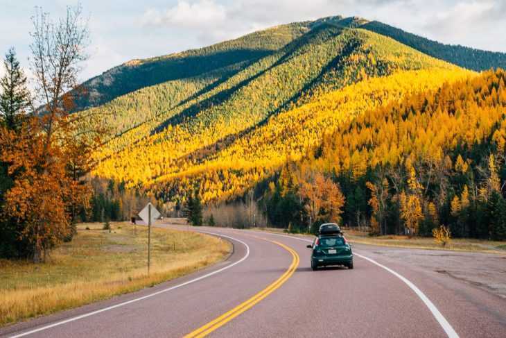 Automobilis, važiuojantis keliu su rudens spalvomis medžiuose