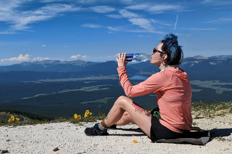   Pārgājiens kalnu pārejas virsotnē dzer ūdeni no Smartwater pudeles