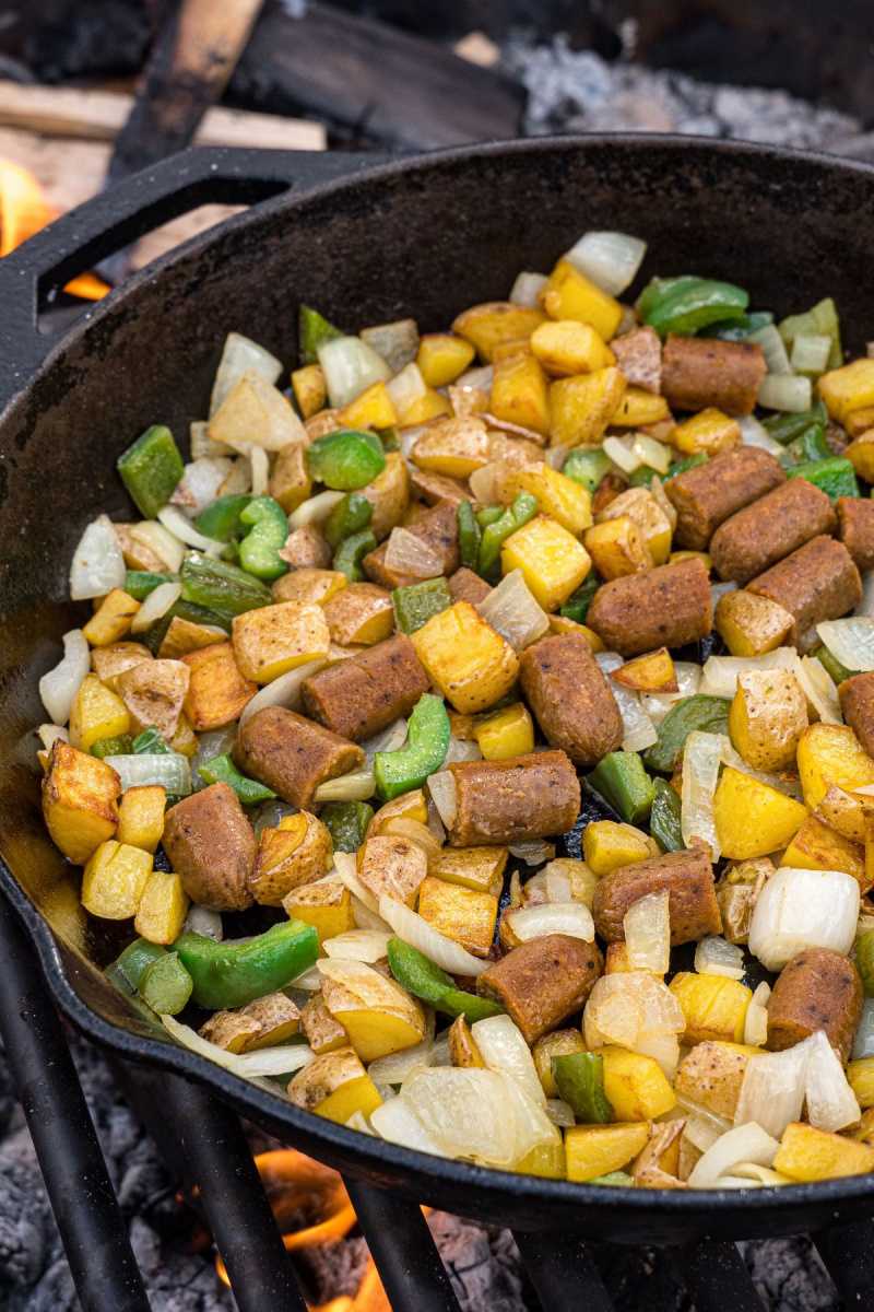   Колбаса, перец, лук и картофель готовятся в чугунной сковороде