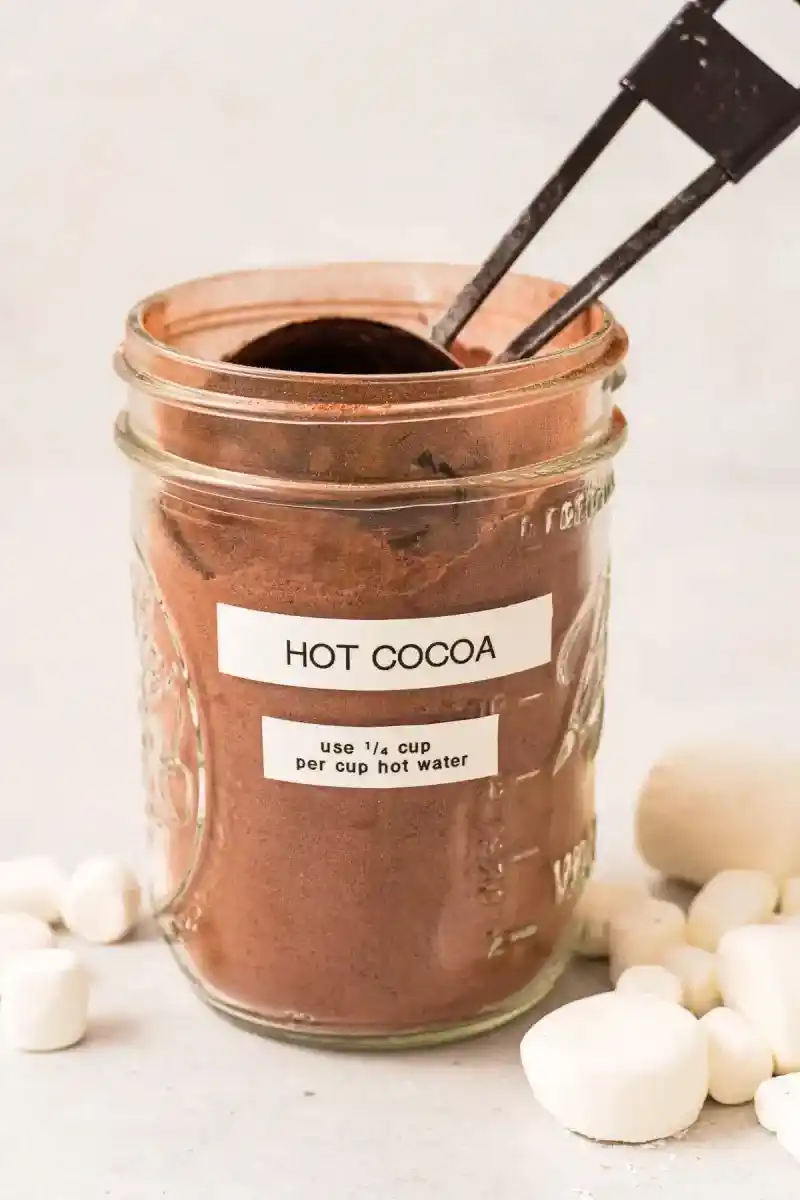   गर्म कोको के साथ एक मेसन जार और अंदर एक ¼ कप स्कूप। लेबल पर लिखा है 'गर्म कोको, प्रति कप गर्म पानी में ¼ कप गर्म कोको का उपयोग करें।'