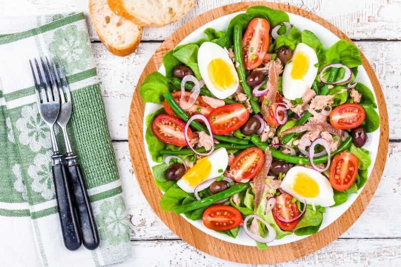   Salată Nicoise cu ouă feliate, ton, roșii și verdeață pe farfurie.