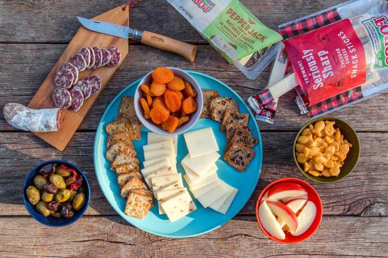   Ost, frukt, salami, nøtter og kjeks vises på et campingbord.