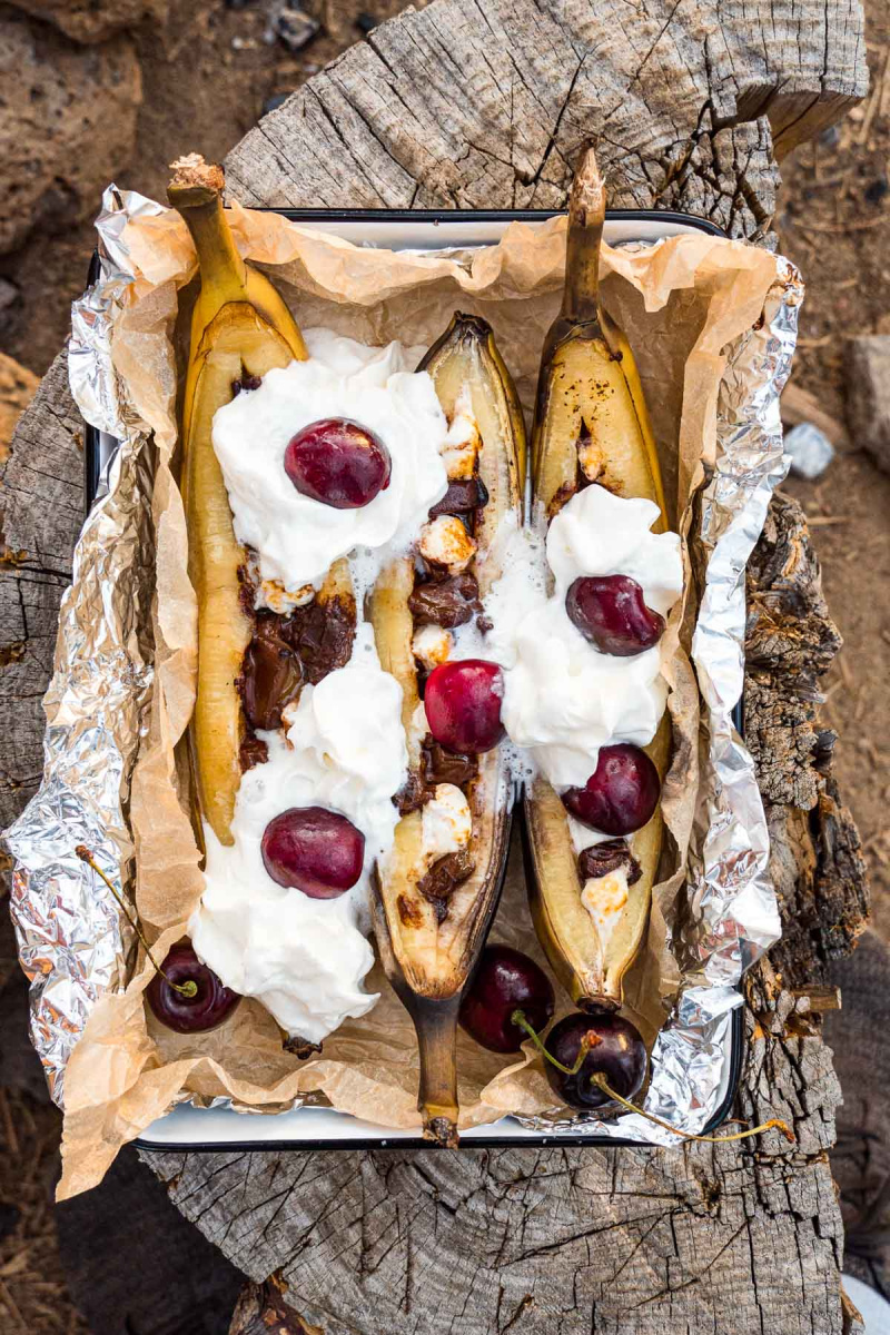   Banana splits au feu de camp garnies de crème fouettée dans un plat de service sur une bûche