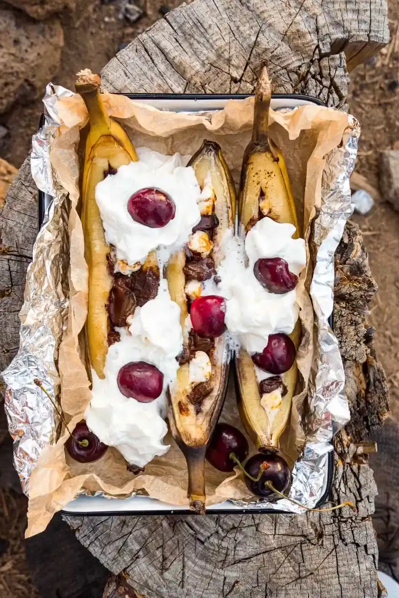   Feuilles de banane sur feu de camp garnies de crème fouettée dans un plat de service sur une bûche