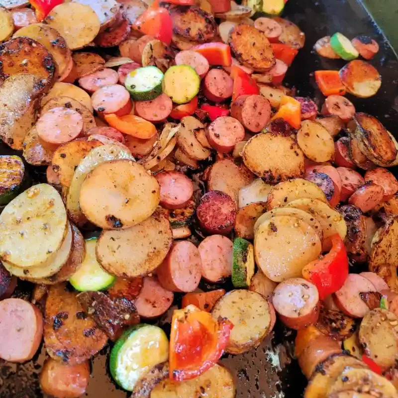   Salsichas, batatas e abobrinha em uma frigideira.