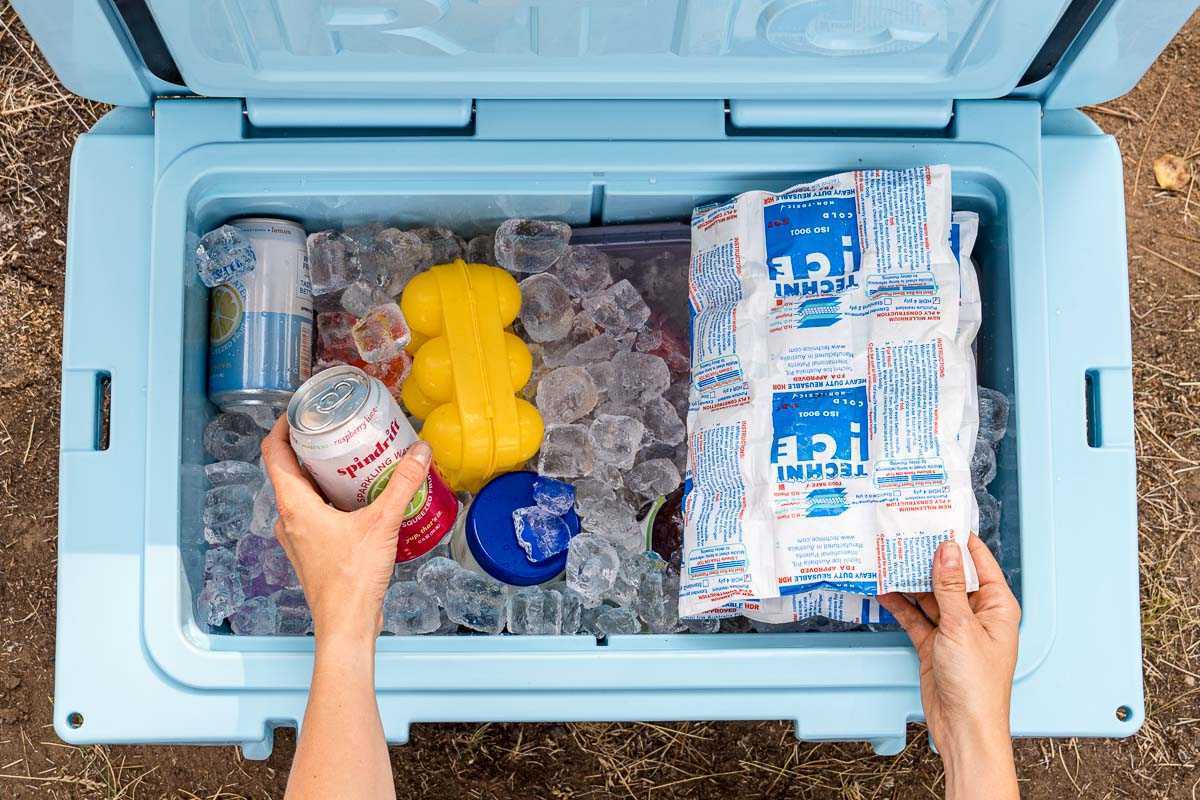 Τα χέρια απλώνουν σε ένα μπλε ψυγείο γεμάτο πάγο για να σηκώσουν ένα κουτί ποτού