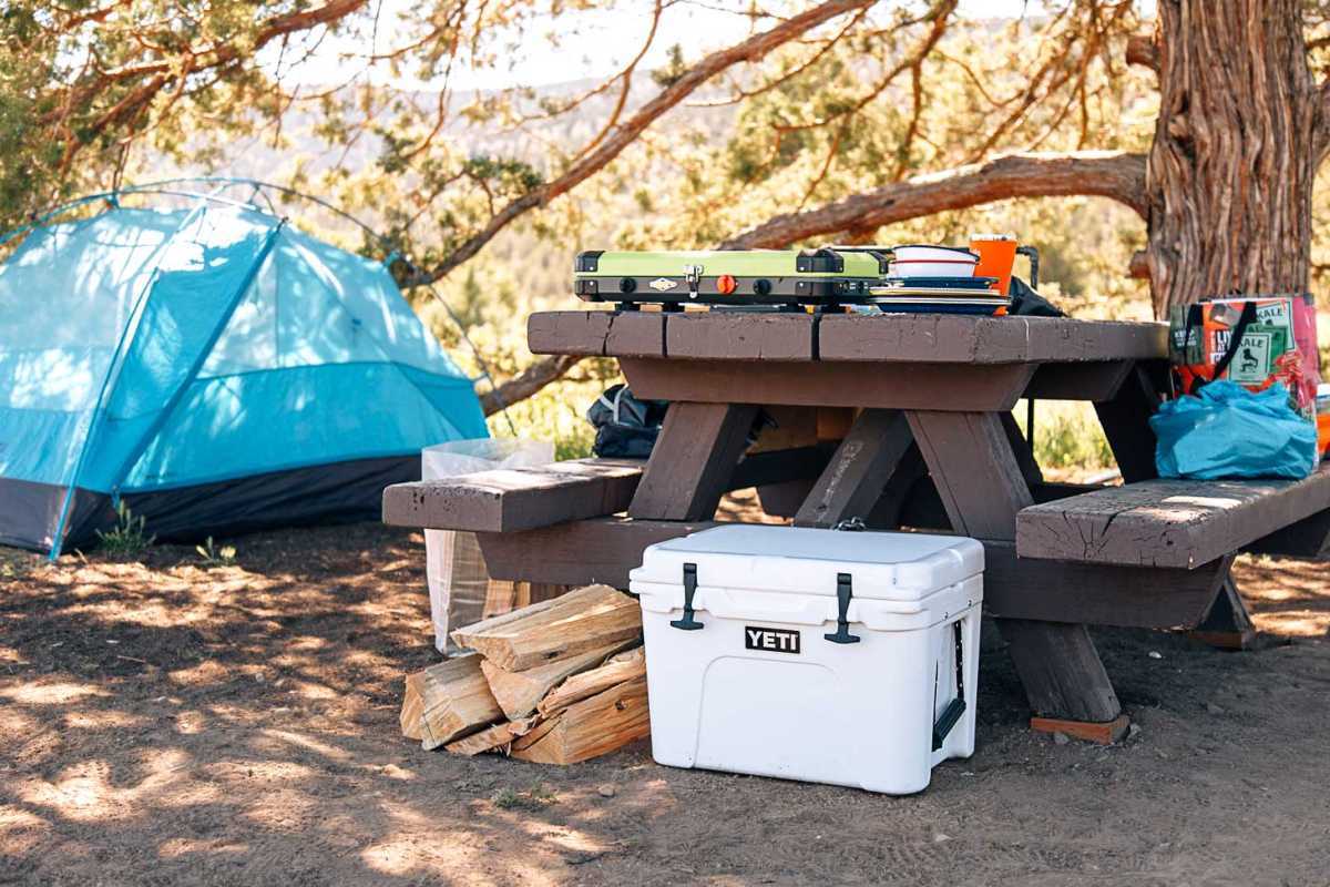 Hladilnik pod mizo za piknik s šotorom v ozadju.