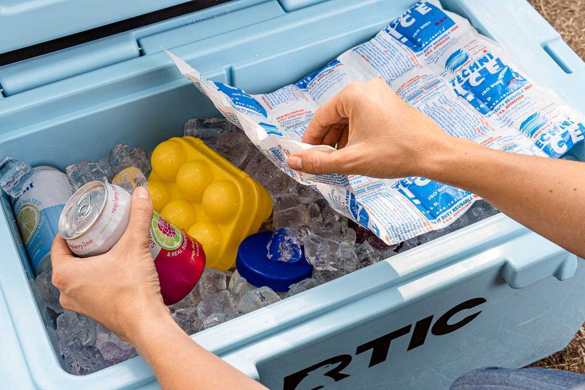 Mãos alcançando um refrigerador azul cheio de gelo para pegar uma lata de bebida