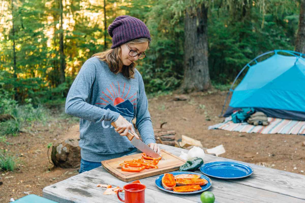 Megan dempeus a una taula de campament picant pebrots vermells sobre una taula de tallar de fusta