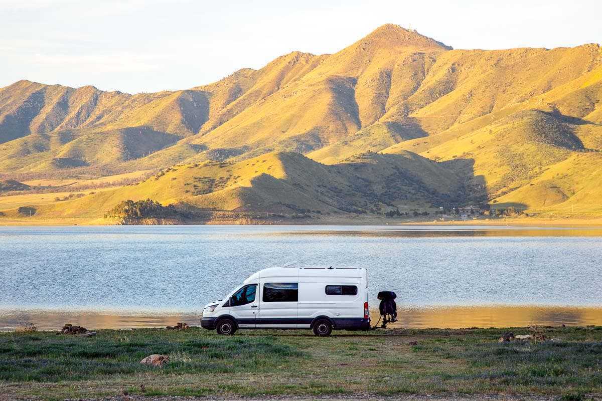 Un camping-car blanc garé devant un lac avec une colline herbeuse en arrière-plan
