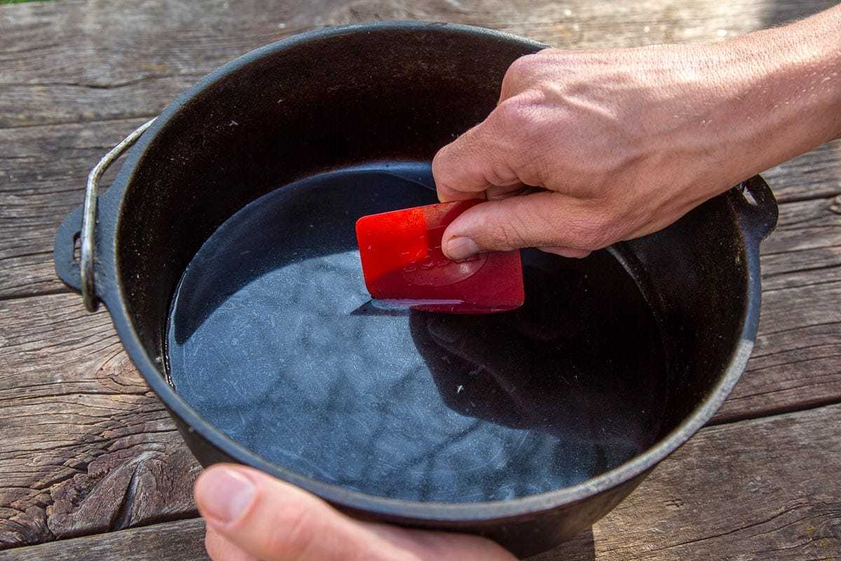 مائیکل پانی سے بھرے ڈچ تندور کو صاف کرنے کے لیے سرخ برتن کھرچنے والا استعمال کر رہا ہے۔
