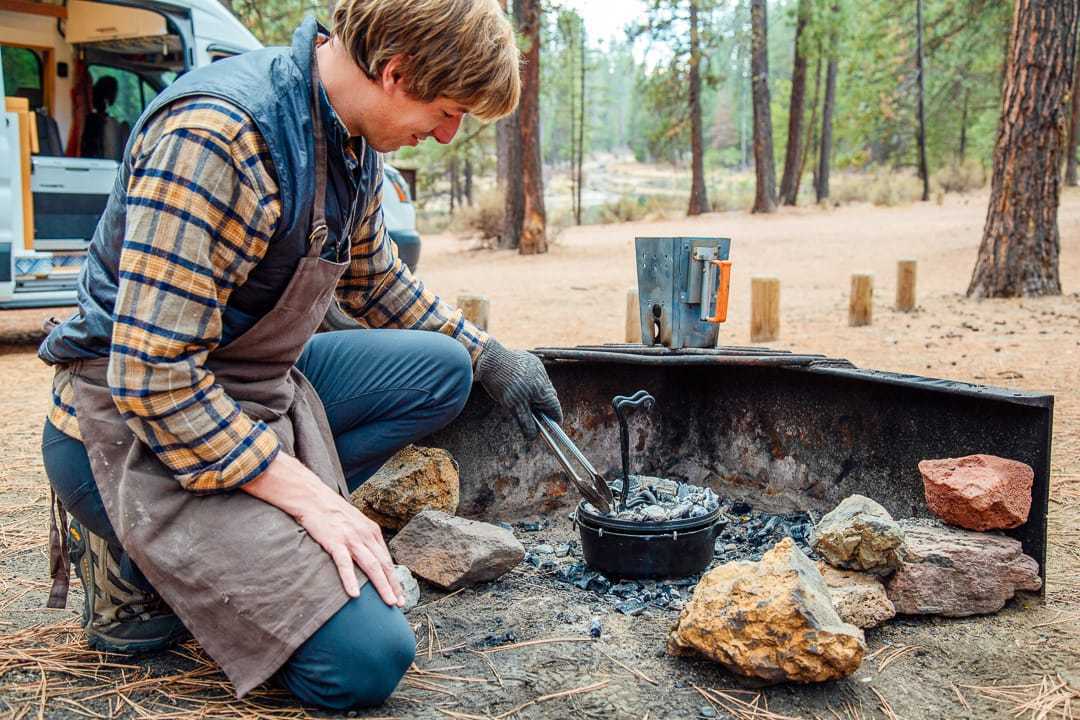Michael utilise des pinces pour placer des charbons de bois sur un faitout de camping