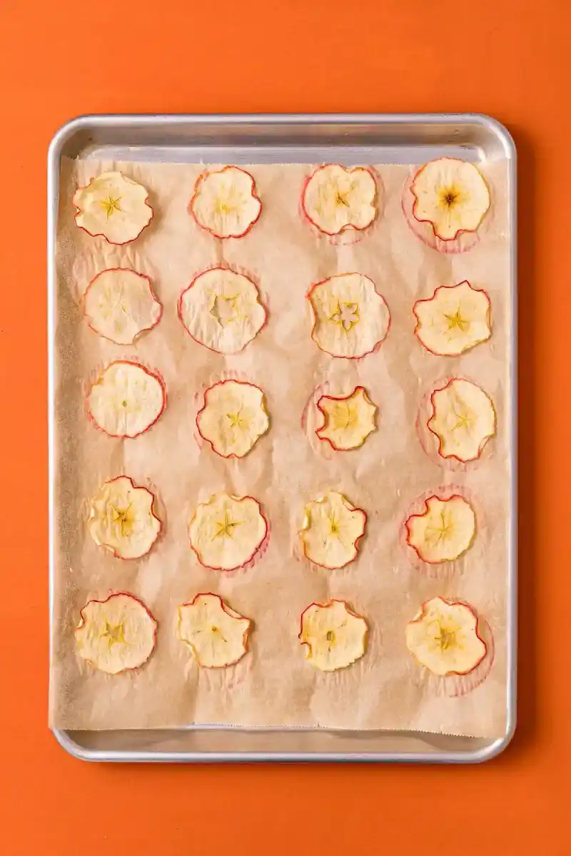   Chips de pommes séchées sur une plaque à pâtisserie tapissée de papier parchemin.