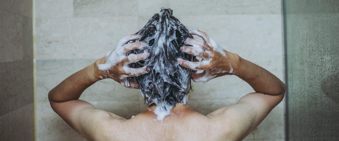 En mann som vasker håret med en sjampo i en dusj
