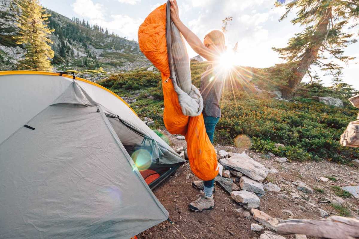 Megan sırt çantalı bir çadırın önünde uyku tulumunu havalandırıyor