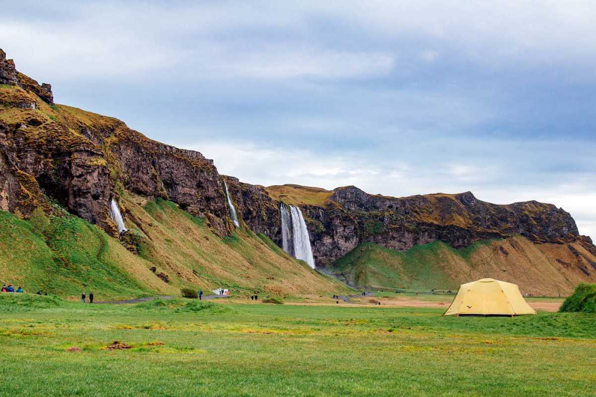 Một chiếc lều màu vàng trên cánh đồng với nền là thác Seljalandsfoss