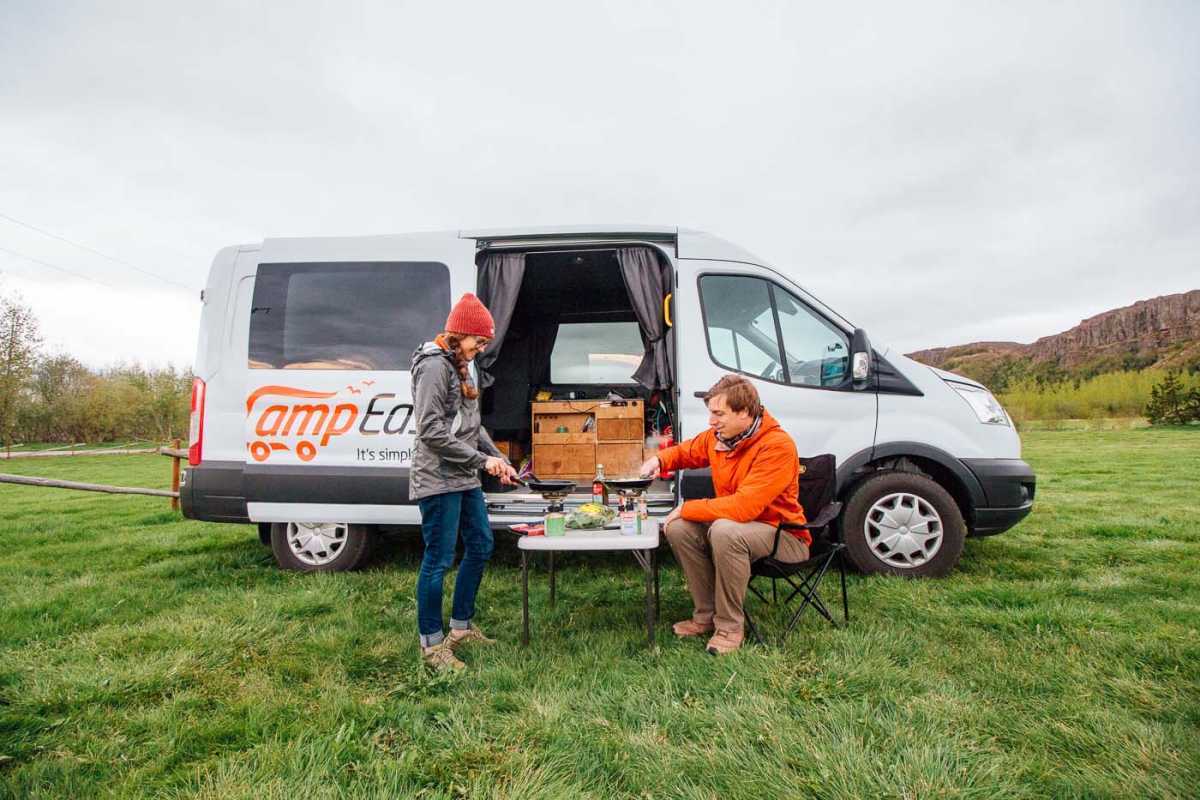 Pariskunta kokkailee pienellä pöydällä Camp Easyn matkailuauton edessä Islannissa
