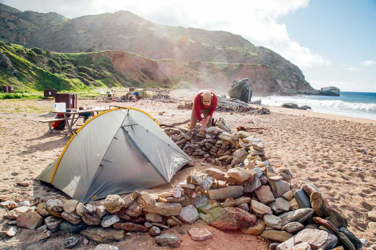 Vīrietis veido akmeņu sienu ap telti.