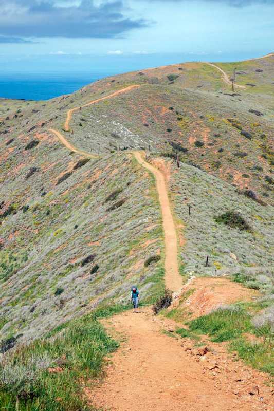 Sieviete brauc ar mugursomu stāvā kalnā pa Trans Catalina Trail