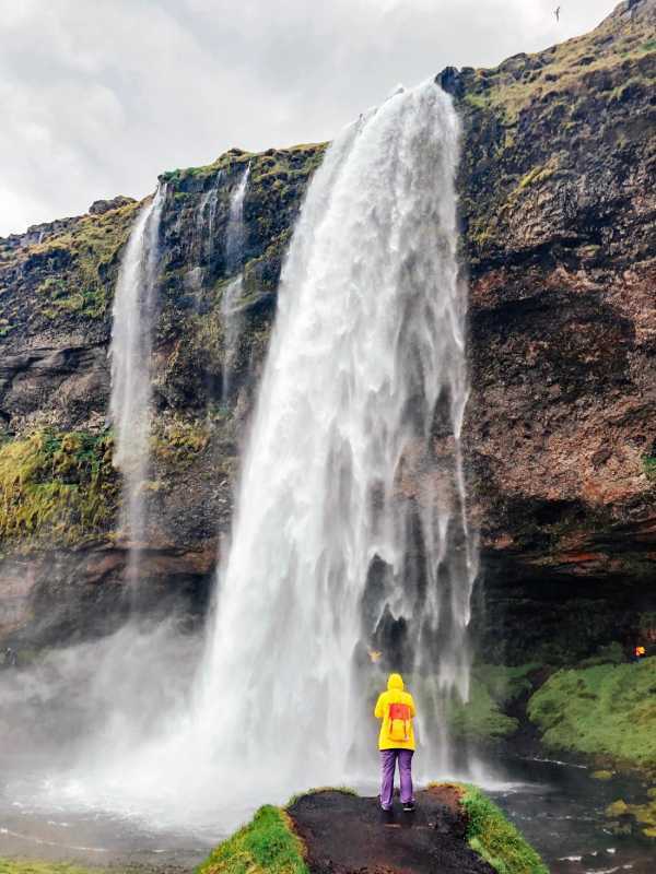 Kollase vihmamantliga naine seisab Seljalandsfossi joa ees