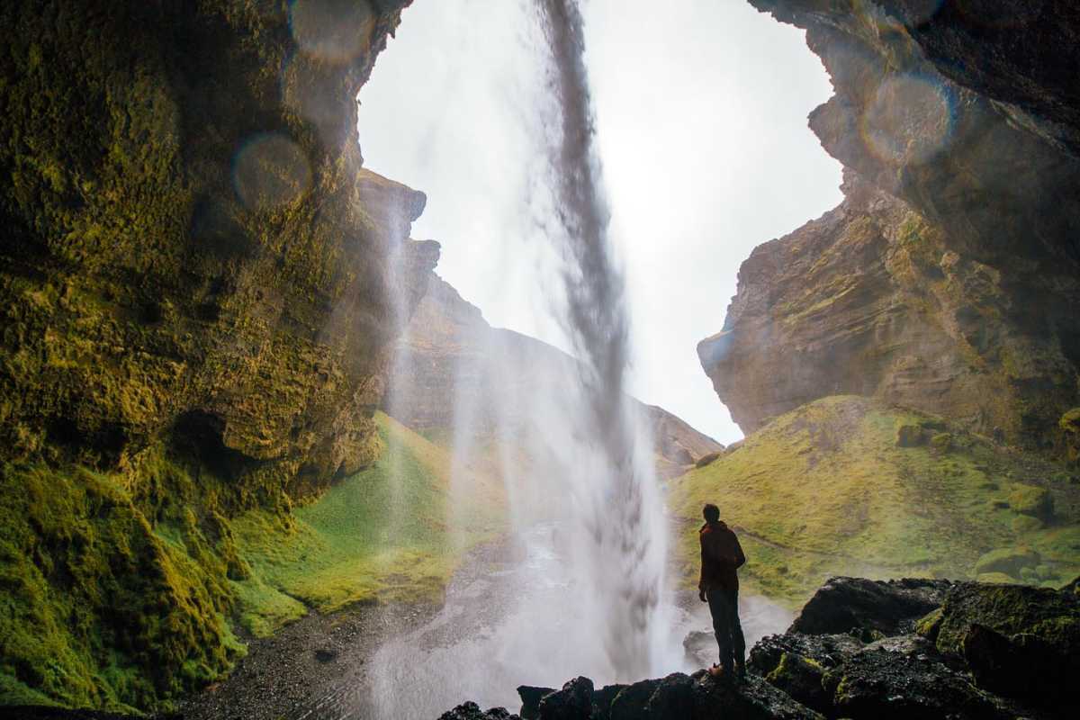 Muž stojaci pod vodopádom Kvernufoss
