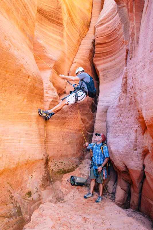 Dvaja muži s canyoneerskou výbavou v oranžovo-ružovom štrbinovom kaňone