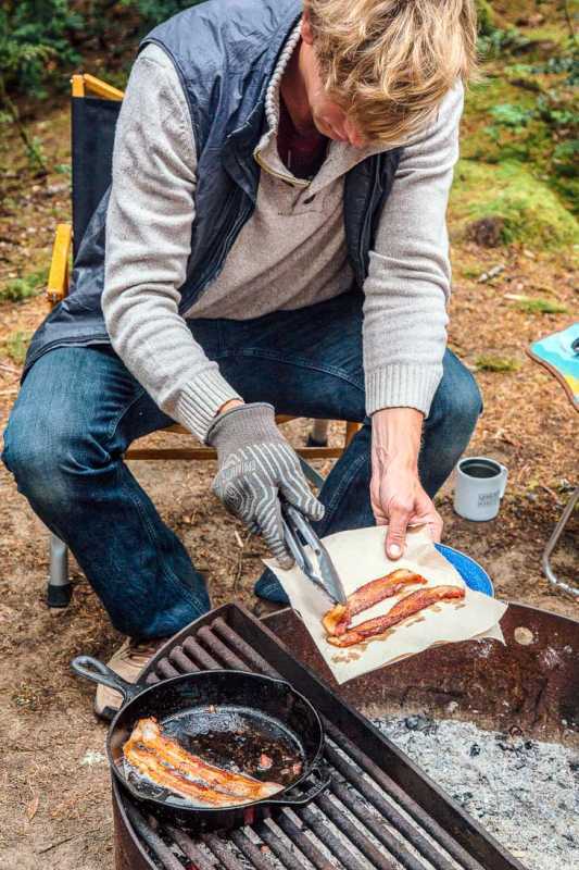 Michael sedí pri táboráku a vypráža slaninu na liatinovej panvici.