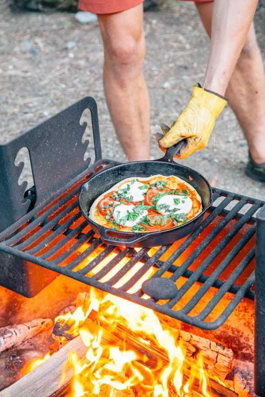 Michael colocando uma pizza em frigideira de ferro fundido sobre a fogueira