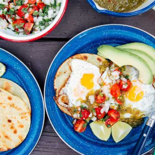 Яйца, салса и авокадо върху тортили върху сини чинии за къмпинг.
