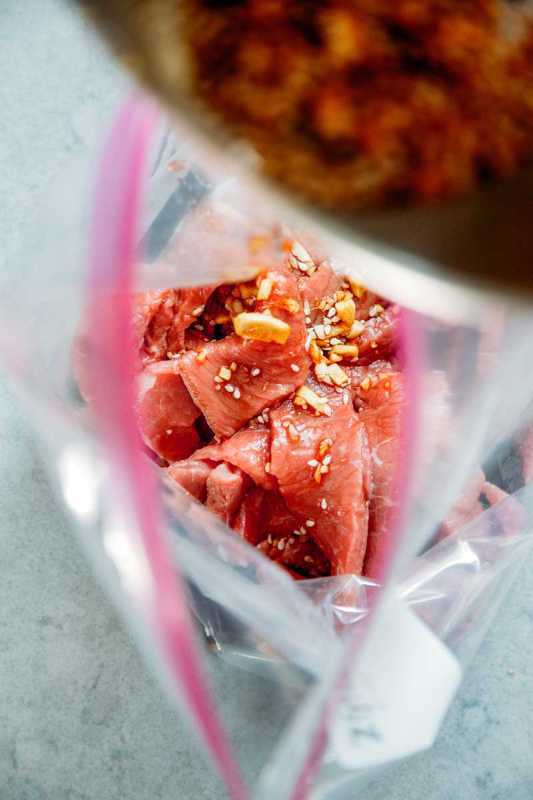 Υπερυψωμένη άποψη της σπασμωδικής μαρινάδας που χύνεται σε μια σακούλα με κομμένο βόειο κρέας.