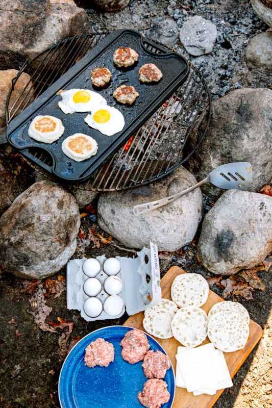 Rissóis de salsicha de ovos e muffins ingleses cozinhando em uma grelha de fogueira
