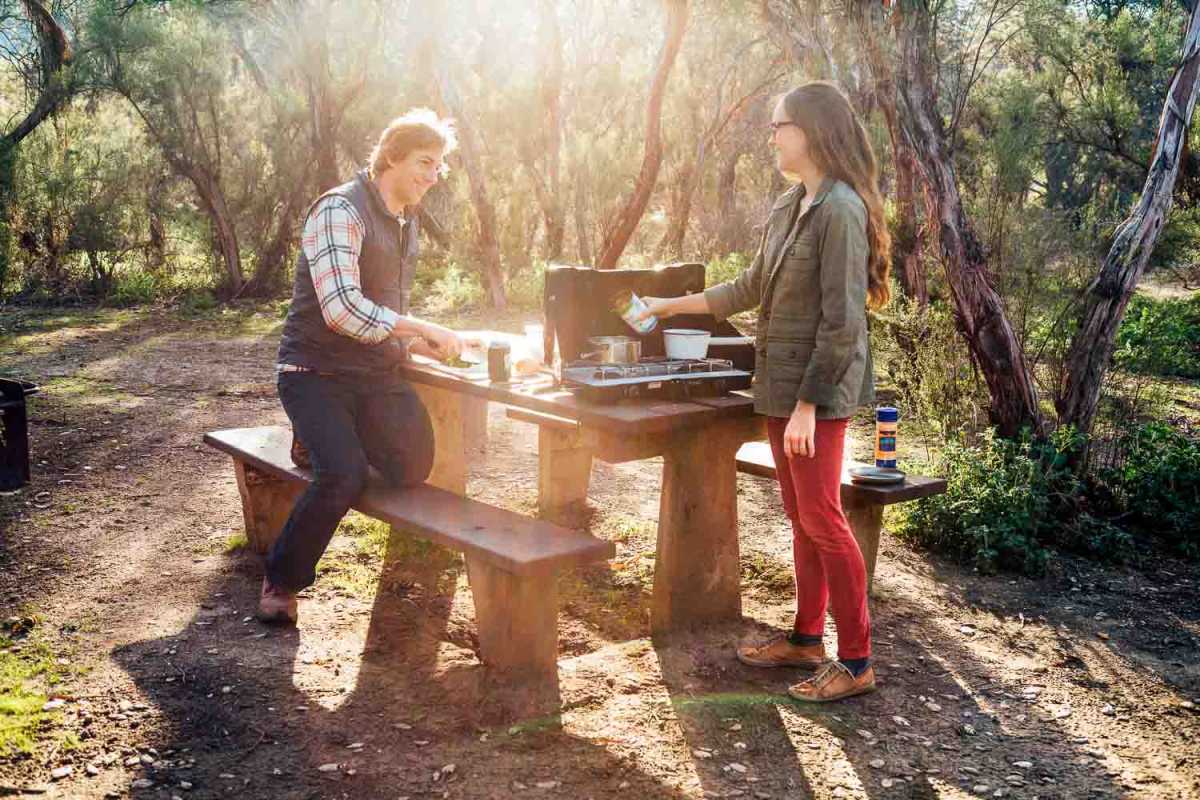 Vyras ir moteris stovyklavietėje gamina maistą ant stovyklavietės viryklės.